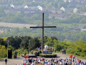 Menschen auf einem Berg vor einem großen Kreuz
