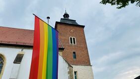 Fahne in Regenbogenfarben vor einer Kirche